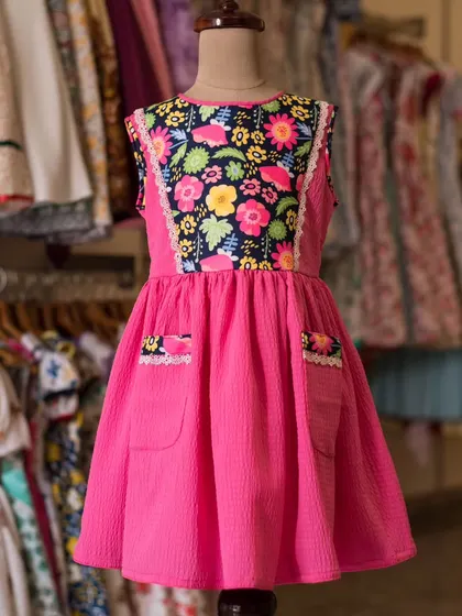 A vibrant pink dress with a bold floral panel on the bodice. The addition of pockets with matching floral trim makes this dress both stylish and practical for little adventurers.