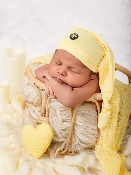 A full portrait of a newborn sleeping in a basket, with soft lighting from prop candles creating a warm and gentle atmosphere.