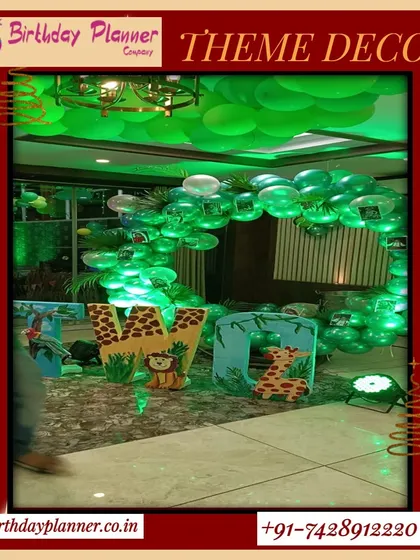 This jungle theme setup features a ceiling covered in green balloons to mimic a forest canopy, along with large, decorated initial letters and animal cutouts for a fully immersive effect.
