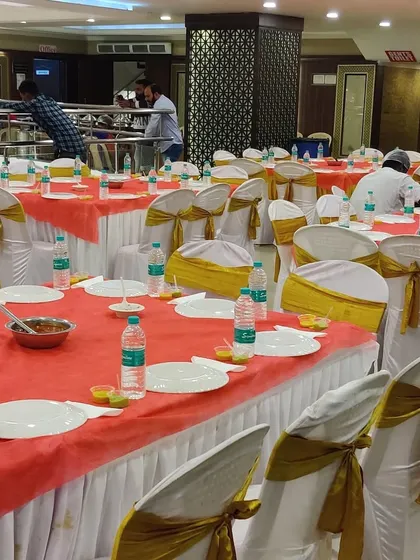 A dining area setup with white and gold chair covers. Our team is seen in the background, making final preparations before the start of the event.