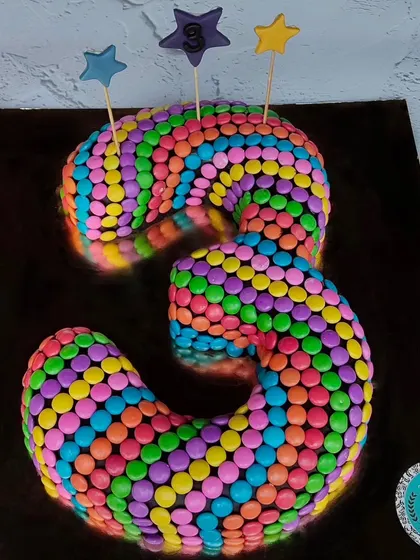 A vibrant number "3" cake covered entirely in colorful Cadbury Gems. This is a fun and eye-catching design that kids absolutely love.