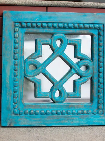 Here is the square carved mirror in a bold turquoise finish, shown against a rustic brick background. This view highlights how the vibrant color and distressed texture can add an unexpected and artistic element to your indoor or outdoor living spaces.