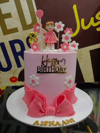 A chic 3kg pink cake with a large fondant bow and a delicate girl figurine topper.