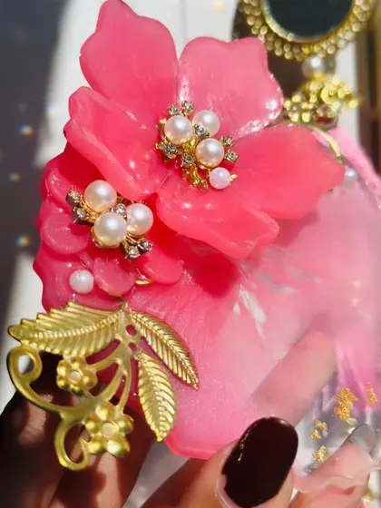 A close up shot showing the detail on a floral Milni plate. You can see the layers of resin, the delicate pearls set in the flower's center, and the intricate golden metal charms.