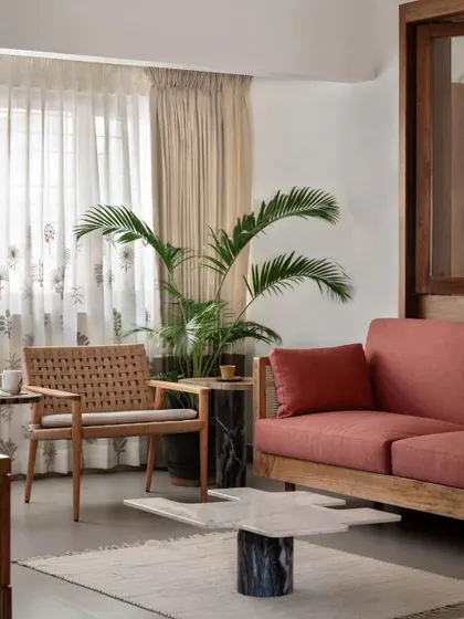A detail of the family lounge, showing the enlarged windows and delicate drapes that enhance the room's light and visual appeal. The furniture includes a comfortable sofa and a woven armchair.