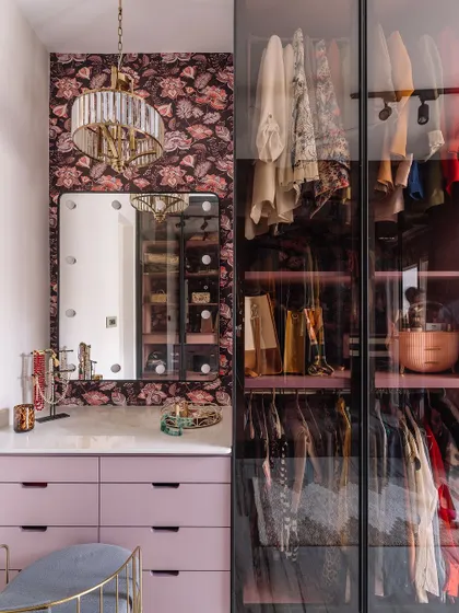 The final look of the chic walk-in closet. The space is now complete with a vanity mirror, elegant chandelier, and glass-door wardrobes, creating a glamorous and highly organized dressing room.