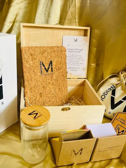 The complete corporate welcome kit. This set includes a branded wooden box, a matching tote bag, a cork notebook, a glass jar, and other custom items for 'Modern Spaaces'.