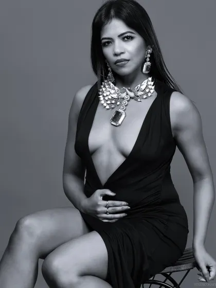 A black and white portrait of a model in a plunging black dress and statement jewellery.