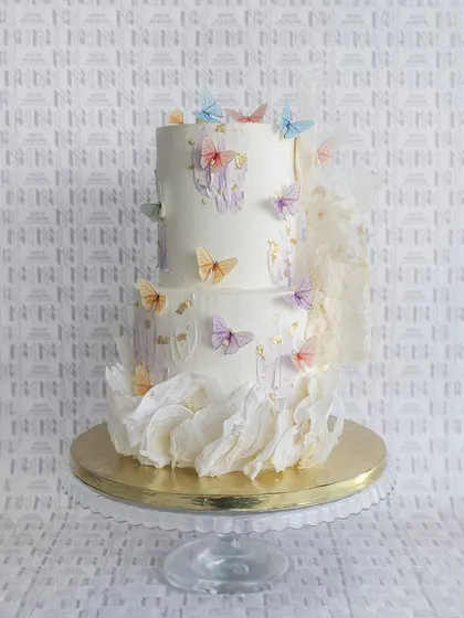 Love takes flight on this enchanting two-tiered wedding cake. It's adorned with delicate, fluttering butterflies and soft, ethereal ruffles for a truly magical look.