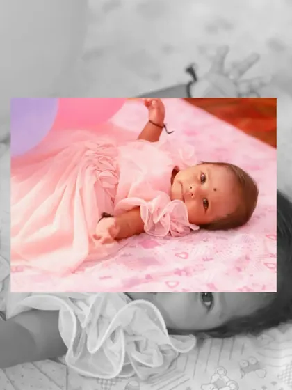 An artistic shot of a baby girl in a pink dress at her naming ceremony, with a black and white overlay.
