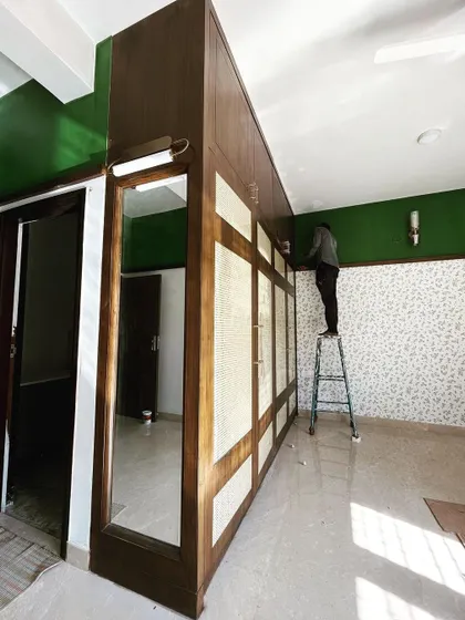 A wider view of the elegant veneer and rattan wardrobe, showing how it integrates with the room's overall design, including the bold green wall and custom lighting.