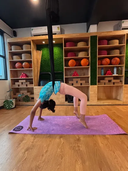 This young yogini uses the hammock to support a beautiful wheel pose. Aerial yoga adds a new dimension to classic poses, making them even more engaging for kids.