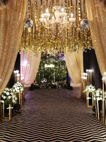 A glamorous entrance tunnel with gold sequin drapes, chandeliers, and a modern black and white carpet.