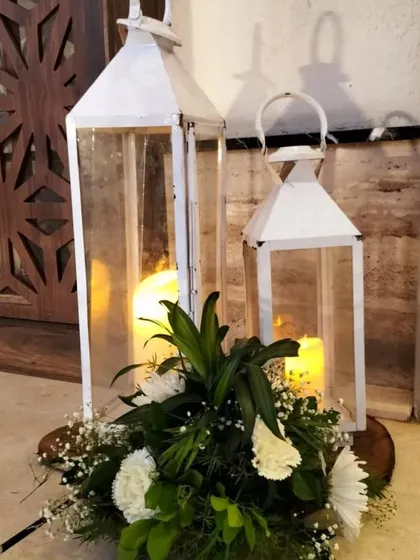 A simple and elegant decor detail. White lanterns with pillar candles are placed on wood slices and surrounded by fresh white flowers and baby's breath.