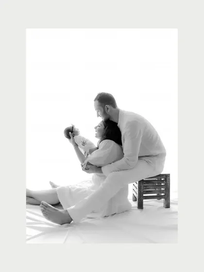 First glimpses of love. A new mother holds her baby up, sharing a moment of connection while the father watches from behind. This black and white newborn portrait is full of emotion.