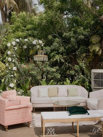 A pleasant pastel lounge area nestled in a lush green corner of the venue, featuring soft pink sofas and armchairs for a relaxed, intimate feel.