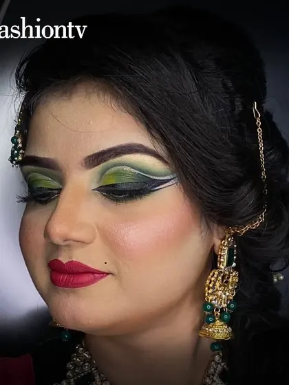 A close-up of a student's work on an advanced bridal look, featuring a sharp, graphic winged eyeliner with a green and black gradient, demonstrating precision and creativity.