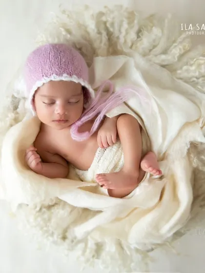 This little one is nestled in a cozy basket lined with soft wool. The light purple bonnet adds a gentle pop of color to this peaceful newborn portrait.
