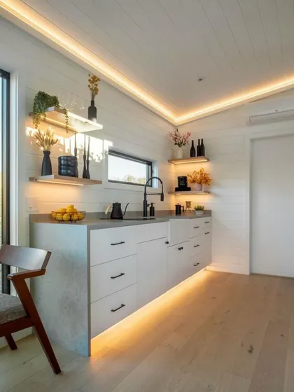 This kitchen design in a compact home shows how floating shelves and under-cabinet lighting can make a space feel open and stylish while providing practical storage.