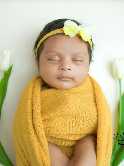 A close-up portrait of the baby in the yellow wrap, focusing on their serene, sleeping face.