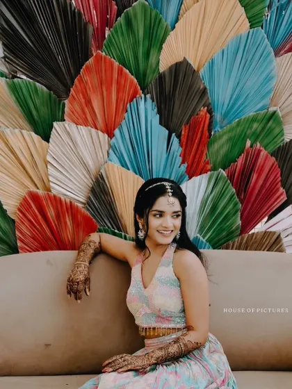 A modern and vibrant Mehendi or Haldi backdrop made of large, multi-colored dried palm leaves, creating a unique and artistic photo corner.