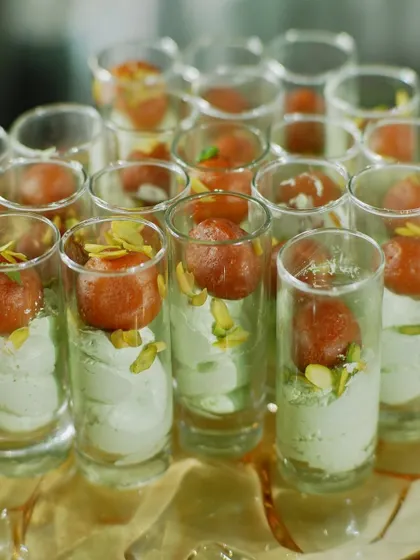 A modern fusion dessert: Gulab Jamun served in a shot glass with a light and airy pistachio cream. This combines a beloved traditional sweet with a contemporary presentation.