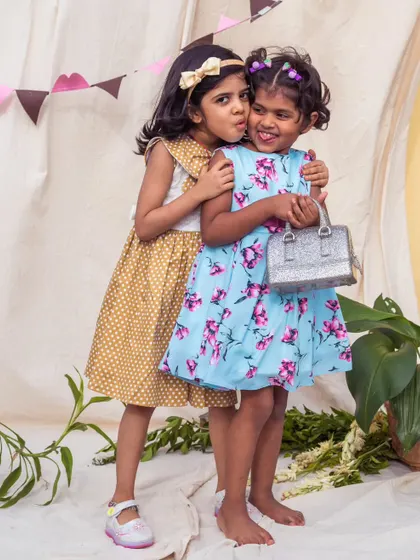A sweet hug between friends. This image showcases a mustard polka dot dress and a blue floral dress, both designed for comfort and style.