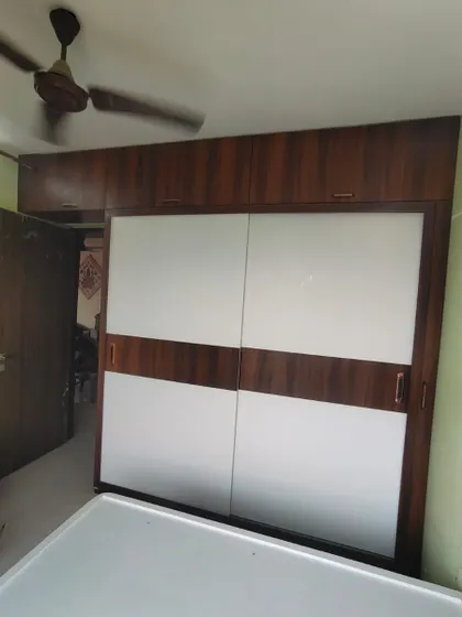 A classic sliding wardrobe with a two-tone design, combining white back-painted glass with a central wooden band.