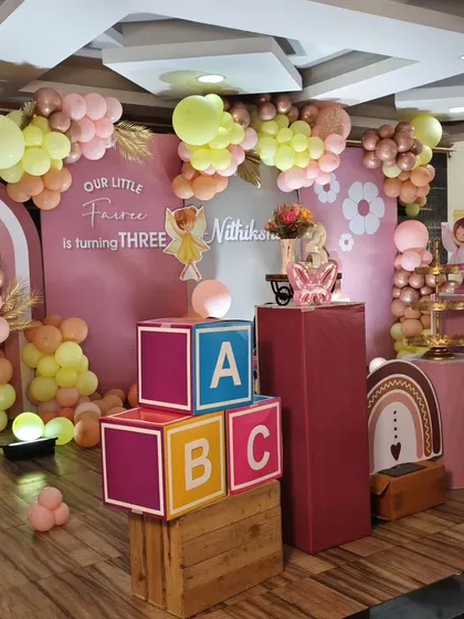 A sweet fairy-themed third birthday party with a pastel pink and yellow balloon garland, rustic wooden crates, and colorful 'ABC' blocks.