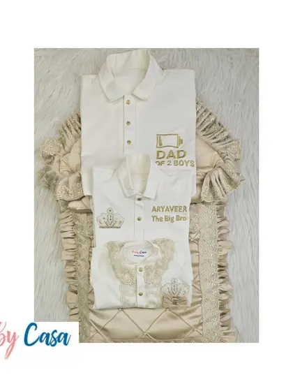 A flat lay of the "Dad of 2 Boys" coordinated set. It includes a newborn romper and wrap, a matching shirt for the big brother, and a polo for dad, all in a classic cream and gold theme.