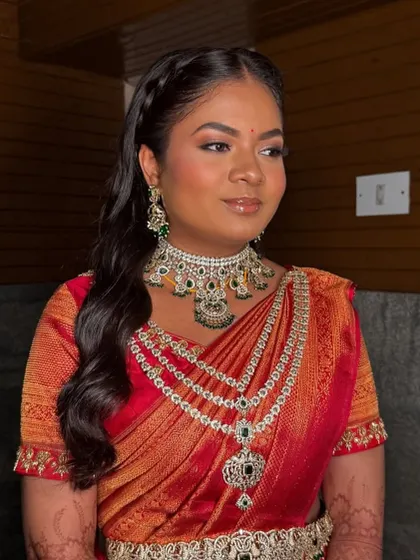 A vibrant reception look in a red saree. The draping is classic, but the modern hairstyle with a side braid gives it a fresh and youthful feel.