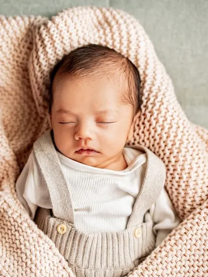 A newborn sleeping peacefully, nestled in a soft pink blanket on the sofa. My at-home sessions mean we can capture these moments wherever your baby is most comfortable.