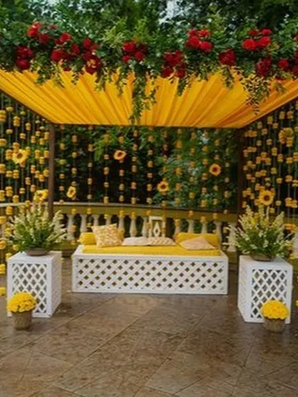 This beautiful outdoor mehendi seating area is covered with a canopy of yellow fabric and hanging marigold strings. The white lattice bench and side tables create a comfortable and picturesque spot for the bride.