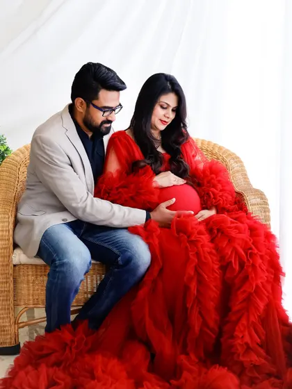 A seated portrait of an expecting couple in our studio. The vibrant red gown and their loving interaction make this a warm and striking photograph.