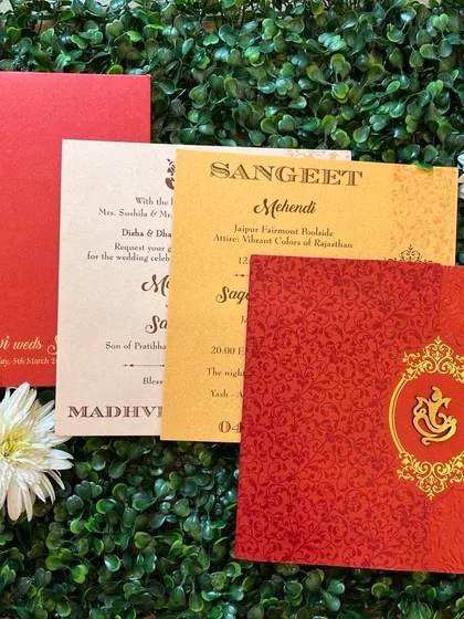 A classic Hindu wedding card set in auspicious red and saffron. The design includes a gold foil Ganesha emblem and separate inserts for the Sangeet and Mehendi ceremonies.