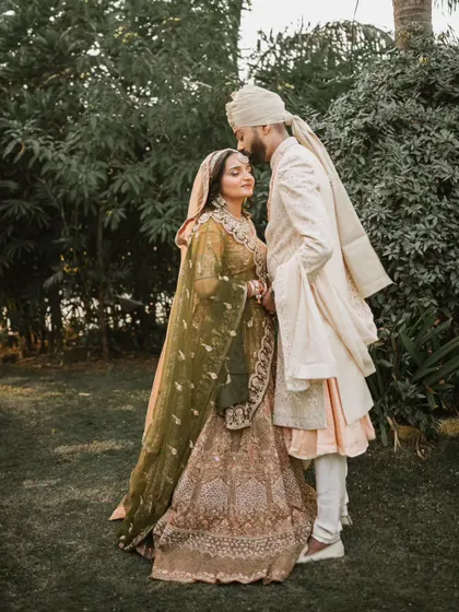 A full-length portrait of the couple in a lush garden setting. The groom’s gentle kiss on his bride's forehead creates a timeless and romantic image.