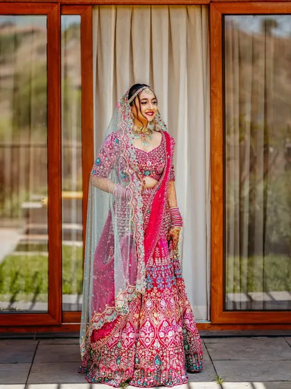 A vision in pink! This stunning full-length portrait showcases the intricate details of the bride's vibrant lehenga. Her happy and confident smile truly lights up the frame.