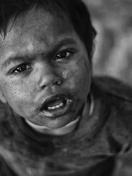 This powerful black and white portrait of a young child looking directly up at the camera is filled with raw emotion. The high-contrast monochrome effect highlights the dirt on his face and the intensity in his eyes, creating a truly unforgettable image.