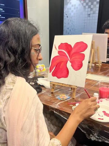 A participant deeply focused on painting a vibrant hibiscus flower. The concentration is a form of meditation.