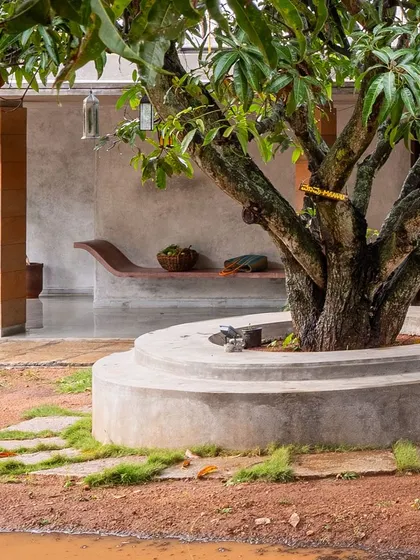 A curved, built-in bench made of ferroconcrete sits under a mango tree at "Aamra." This element serves as another point of rest, inviting residents to slow down and connect with the landscape.