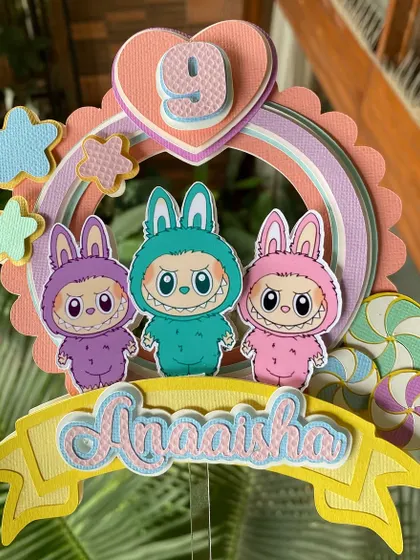 A full view of the personalized Labubu cake topper, showing the custom name banner at the bottom.