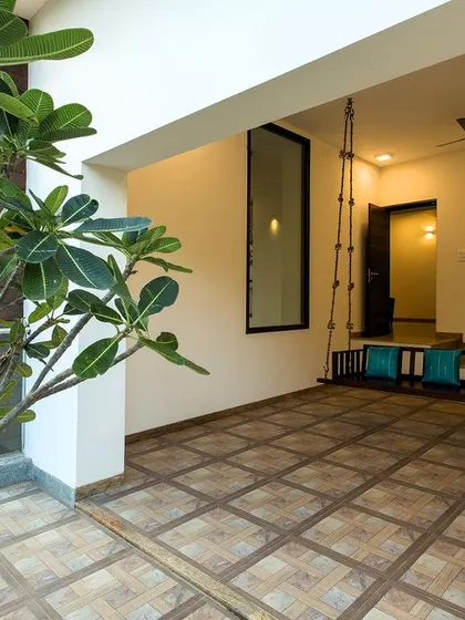 A semi-outdoor veranda space featuring a traditional wooden swing (`oonjal`) and patterned floor tiles, creating a perfect spot for relaxing.