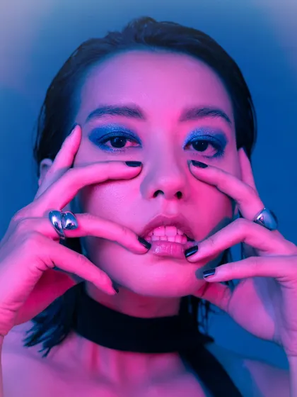 An expressive close-up beauty shot. The colored lighting and the model's pose create a bold and artistic image, perfect for a beauty or fashion editorial.