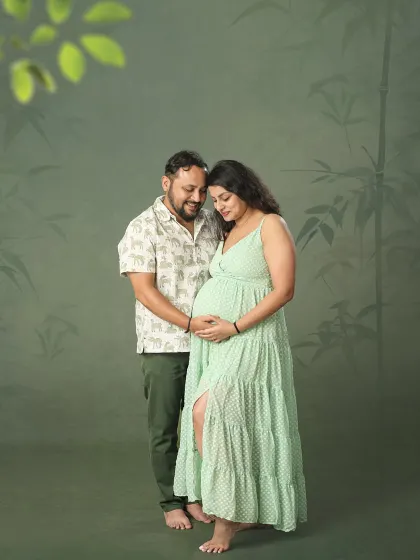 A quiet and connected moment between an expecting couple. Standing together against a green studio backdrop, they look down at the baby bump with love and wonder.