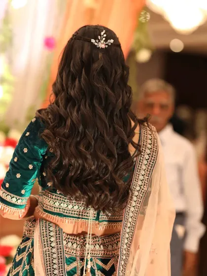 A look at the beautiful, cascading curls and hair accessory for this reception look. The hairstyle was designed to complement her elegant, heavy lehenga.