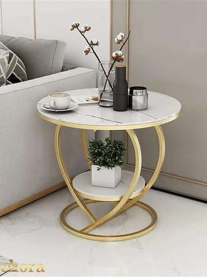This heart-shaped metal coffee table is shown in a living room setting, highlighting its use as a functional side table. The two tiers provide space for both decorative and practical items.