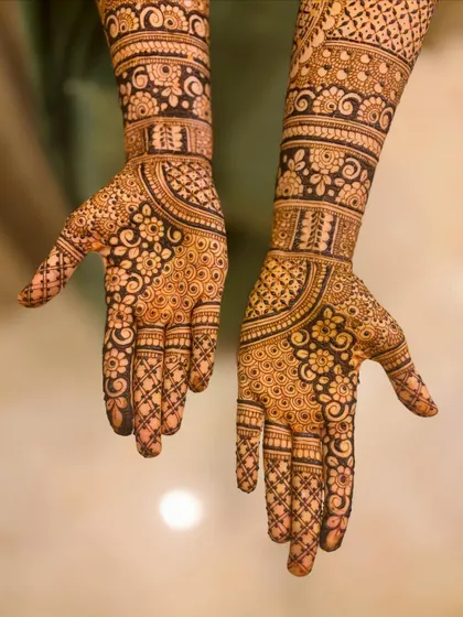 A classic full-hand bridal mehendi with dense, intricate patterns. This design features floral motifs, circular patterns, and detailed work on the fingers.