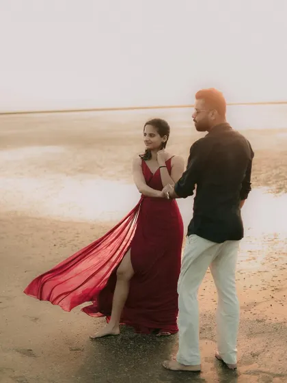 A romantic pre-wedding photo on the beach, with the bride's red dress flowing in the breeze, adding a pop of color and movement.