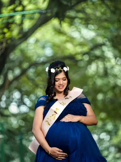 An outdoor maternity portrait in a beautiful park. The mother-to-be is cradling her belly, surrounded by the soft greens of nature.