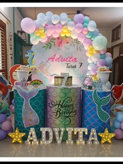 This mermaid-themed party for Advita's 7th birthday features a pastel balloon arch and custom-printed pedestals. The decor includes Ariel cutouts and marquee letters, creating a magical underwater atmosphere right at home.